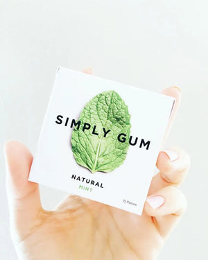 Hand holding a package of Simply Gum with a mint leaf on a white background