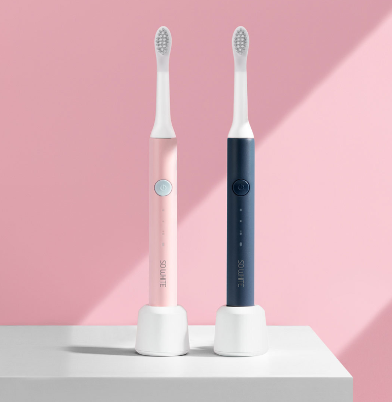Two electric toothbrushes, one pink and one blue, on a white platform with a pink background.