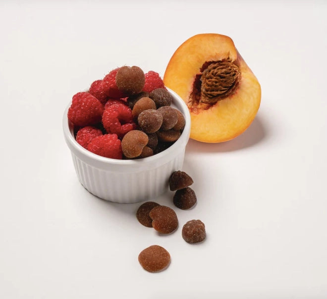 Small white bowl with raspberries and chocolate truffles next to a peach on a light background