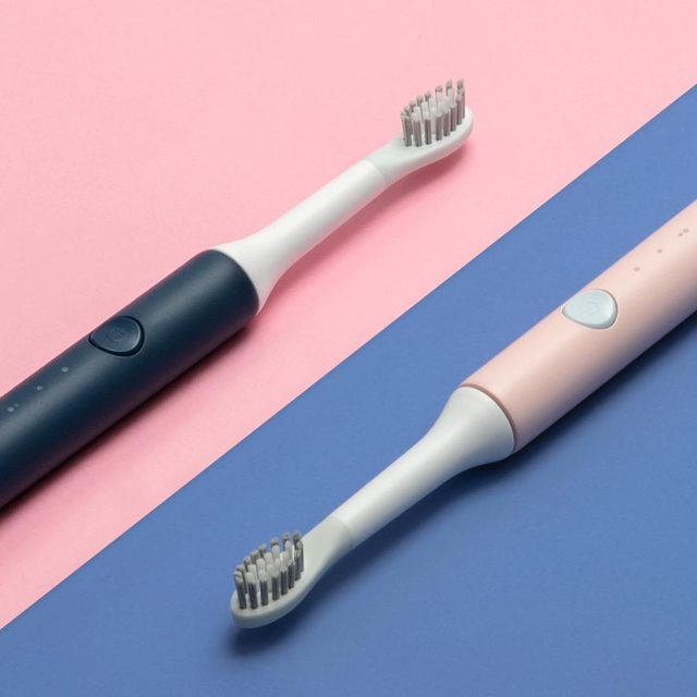 Two electric toothbrushes, one black and one pink, on a two-tone pink and blue background.