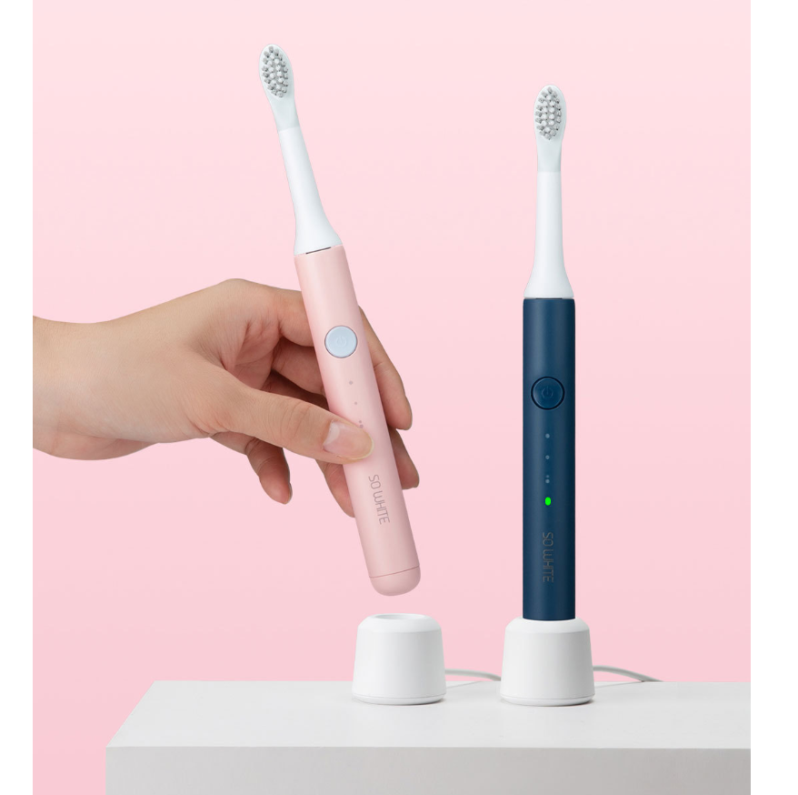 Pink and blue electric toothbrushes with a hand holding one against a pink background