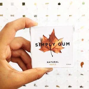 Hand holding a box of 'Simply Gum' with a maple leaf design on a light background.