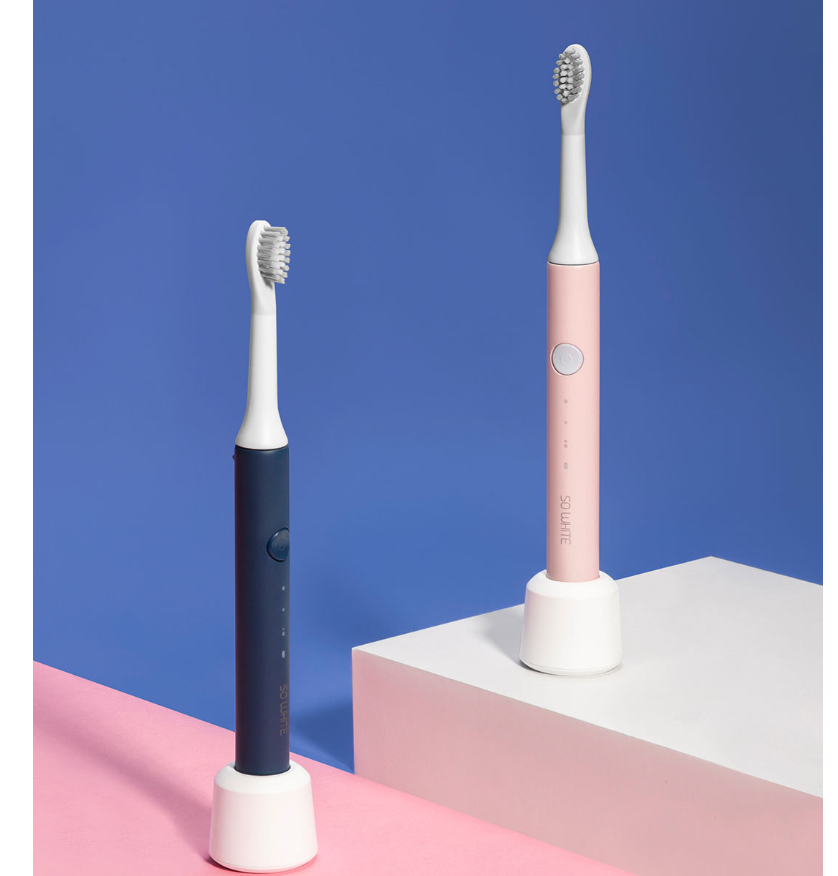Two electric toothbrushes, one black and white, the other pink and white, on a blue and pink geometric background.