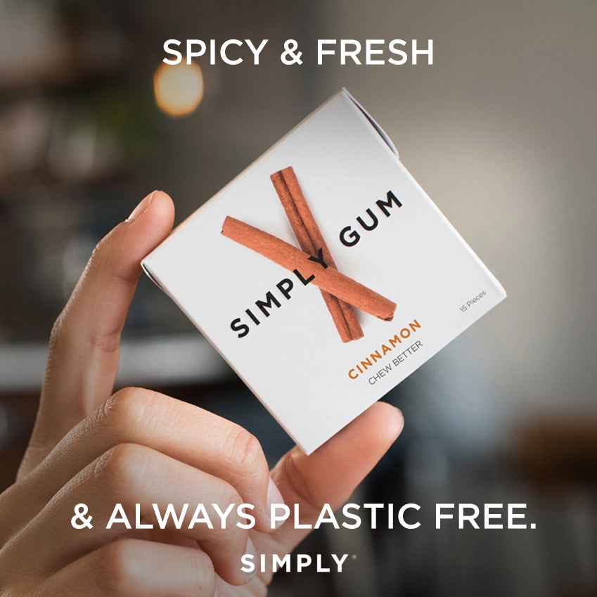 Hand holding a box of Simply Gum with cinnamon sticks on a blurred background