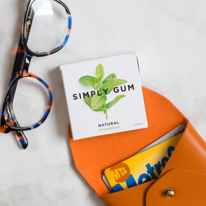 Box of Simply Gum with a pair of glasses and an orange wallet on a light surface