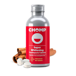 A bottle of CHOMP Super Whitening Toothpaste Tablets with cinnamon sticks and white tablets in the foreground on a white background.