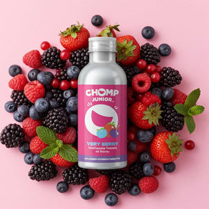 Silver bottle labeled 'CHOMP Junior' surrounded by berries on a pink background