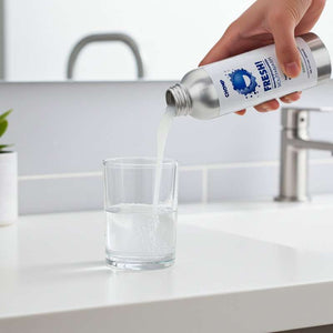 Person pouring water from a bottle labeled 'FRESHii' into a glass on a kitchen counter.