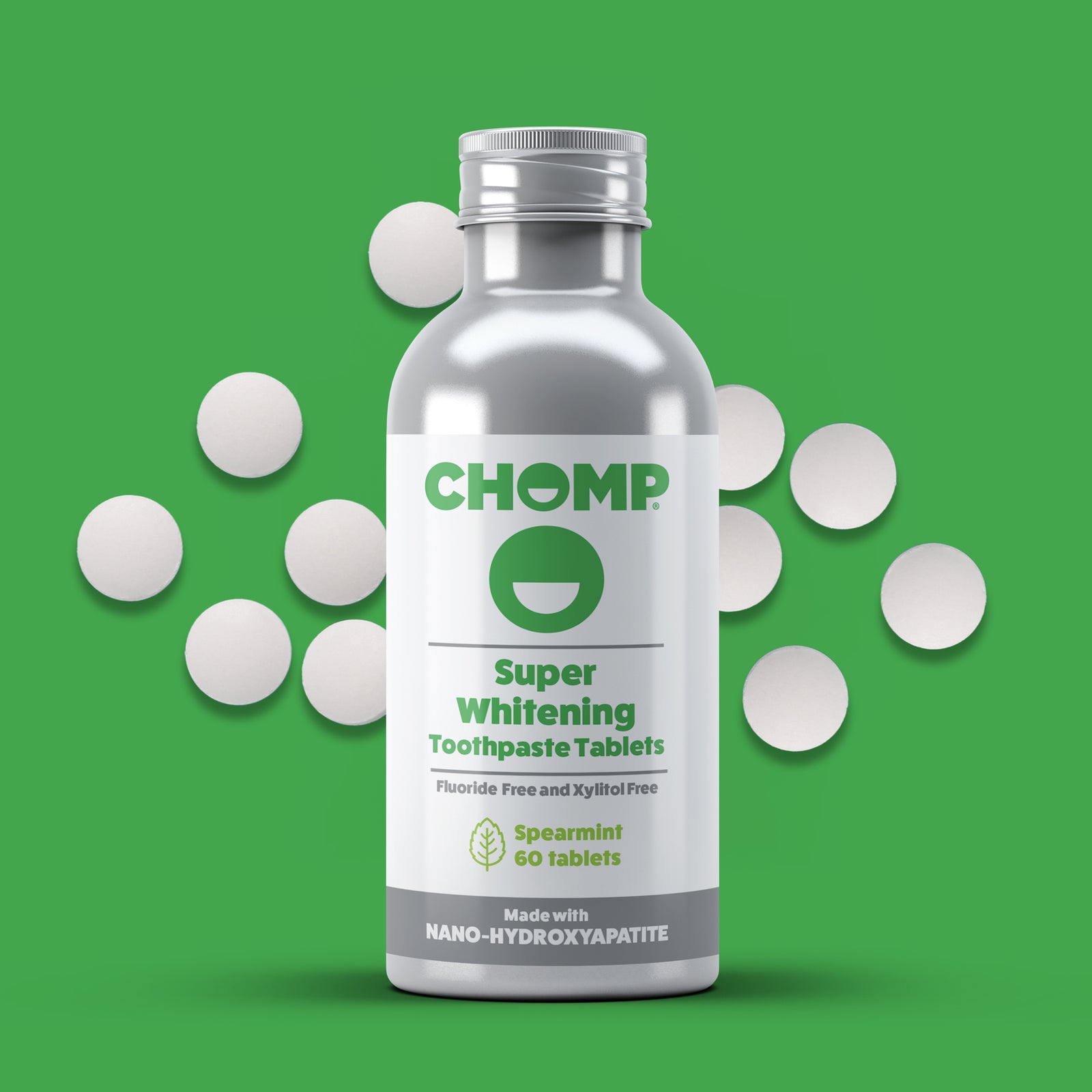 Bottle of CHOMP Super Whitening Toothpaste Tablets on a green background with scattered tablets.