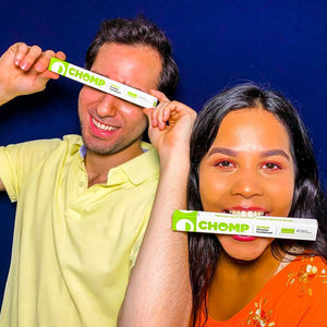 Two people holding 'CHOMP' products in front of their faces against a blue background