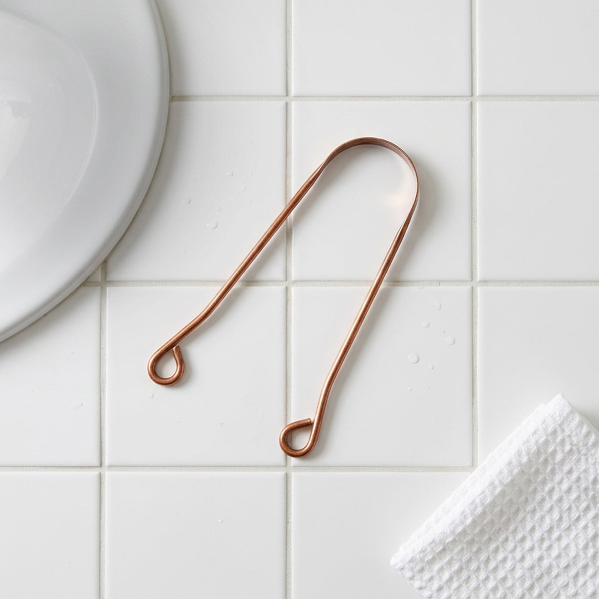 Copper kitchen tool on a tiled surface with a white plate and paper towel in the background.