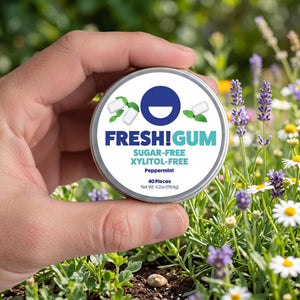 FRESH! gum tin being held by a male hand with an outdoor background of flowers and green grass.