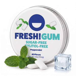 FRESH! gum tin on white surface and background with a mint leaf, ice and two pieces of gum sitting in front.