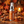 A bottle of CHOMP Pumpkin Spice Fresh Spray stands on a wooden surface surrounded by autumn spices, cinnamon sticks, star anise, small pumpkins, and scattered pumpkin spice powder. The background features blurred fall leaves and a warm glowing lantern.