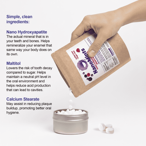 A hand holds a kraft paper pouch of Stumout oral hygiene product above a small metal tin filled with white tablets, with three tablets spilled beside it. Blue text on the left lists ingredients: nano hydroxyapatite, malitol, and calcium stearate.