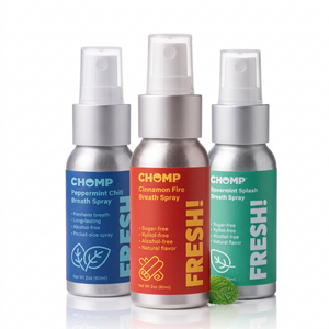 Three CHOMP breath sprays in silver metal bottles with clear caps, shown on a white background: blue Chomp Peppermint Chill Breath Spray, red Chomp Cinnamon Fire Breath Spray, and green Chomp Peppermint Splash Breath Spray. A small mint leaf sits at the base of the center bottle.