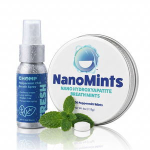 Chomp Peppermint Chill Breath Spray next to a round tin of NanoMints peppermint breath mints, with mint leaves and a single white mint cap on a white reflective background.
