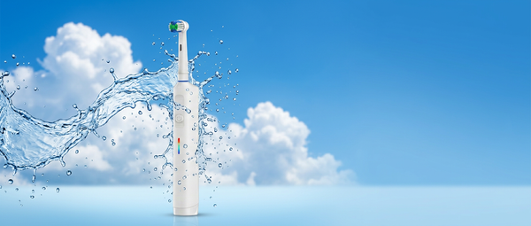 A white electric toothbrush with a green and white bristle head stands upright in a stylized splash scene against a blue sky and clouds background.