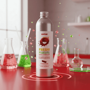 Silver bottle of Chomp Freshi Probiotic Mouthwash on a red surface with laboratory beakers in the background.
