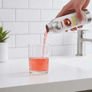 Person pouring pink liquid from a bottle into a glass on a kitchen counter.