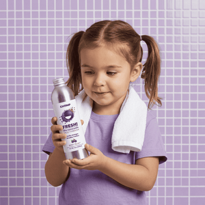 Child holding a bottle of 'Fresh!' mouthwash against a purple tiled wall