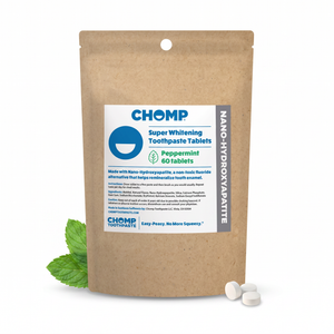 A stand-up kraft paper pouch of CHOMP Super Whitening Toothpaste Tablets in Peppermint flavor, shown on a white background with two white tablets in front and mint leaves at the base of the pouch.