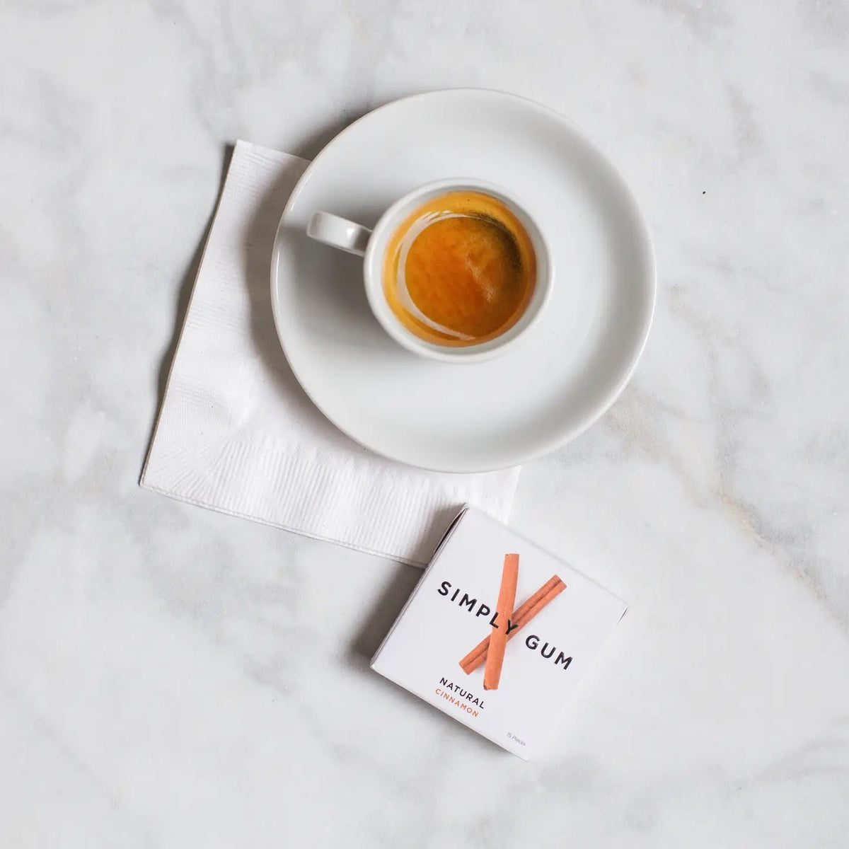 White cup of coffee on a saucer with a box of Simply Gum on a marble surface
