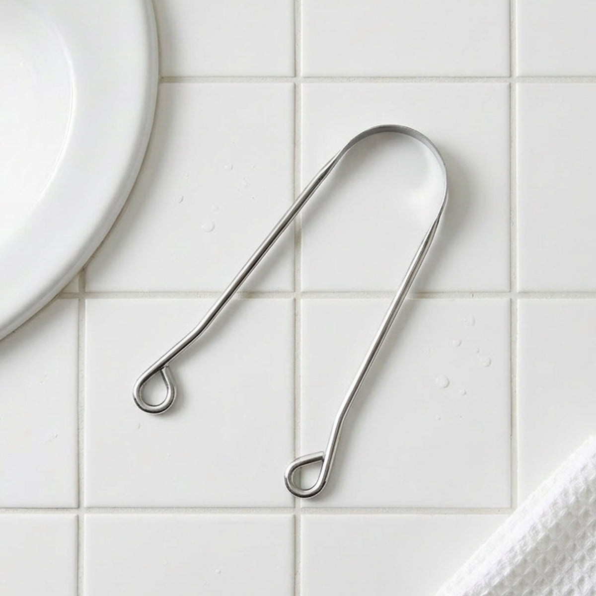 Stainless Steel tongue scrapper on a white tiled surface