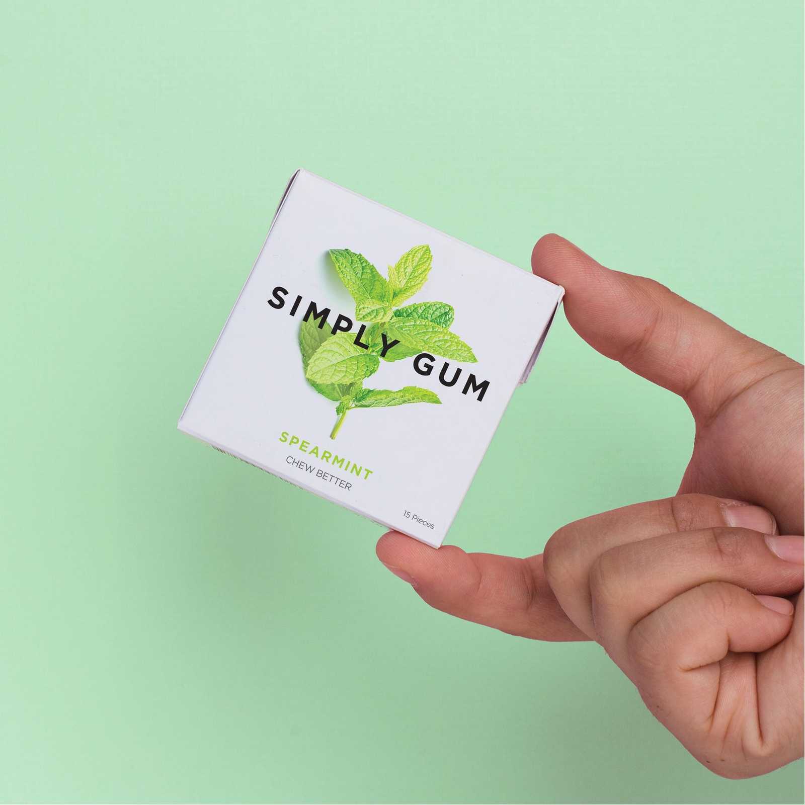 Hand holding a box of Simply Gum with spearmint flavor on a light green background
